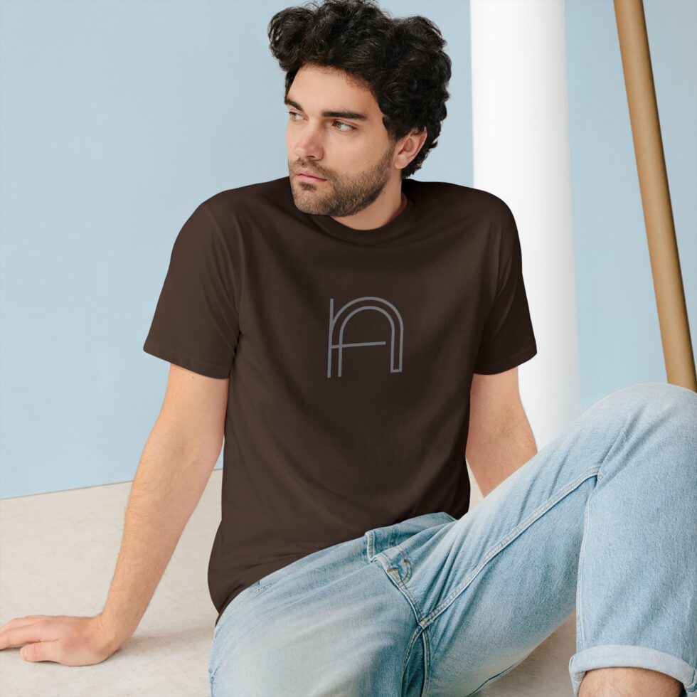 A photo of a young male model sitting wearing a walnut unisex color tee shirt with a grey minimalist NA tee shirt design.