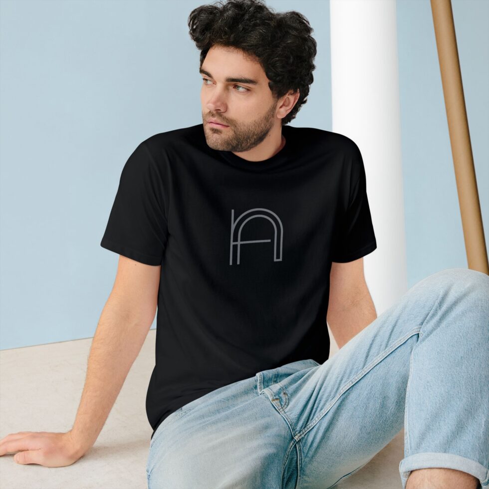 A photo of a young male model sitting wearing a black color tee shirt with a grey minimalist NA tee shirt design.