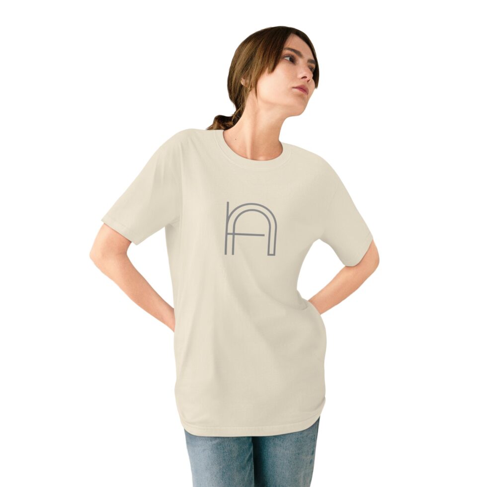 A photo of a young female model wearing a natural color unisex tee shirt with a grey minimalist grey graphic NA tee shirt design.