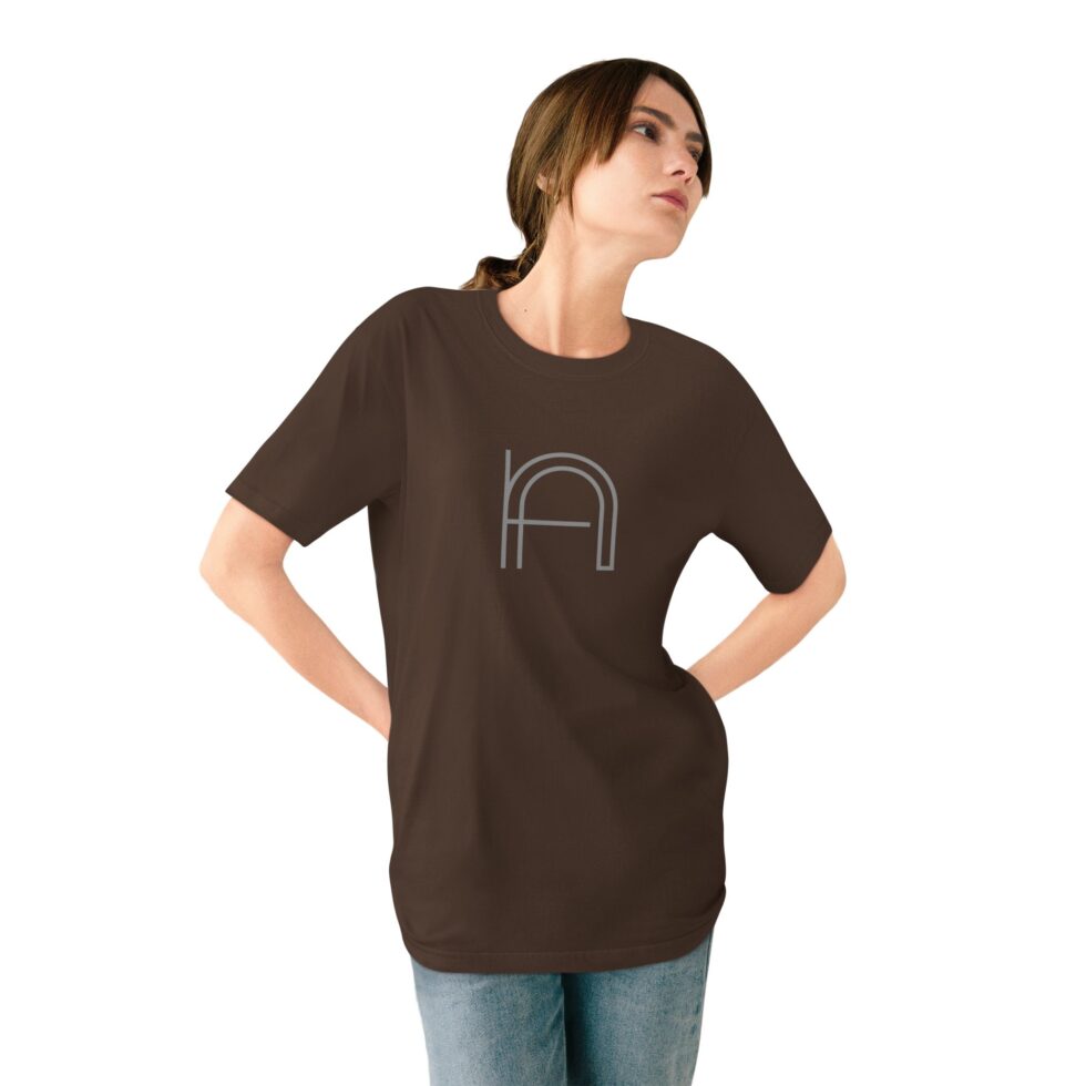 A photo of a young female white model wearing a walnut color unisex tee shirt with a grey minimalist grey graphic NA tee shirt design.